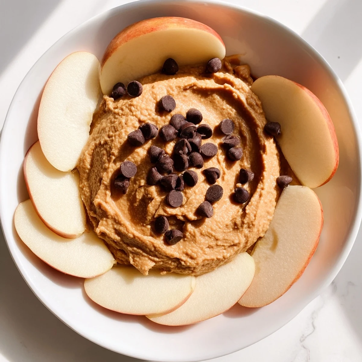 A spoonful of sweet chickpea cookie dough dip with chocolate chips, ready to be served with apples.