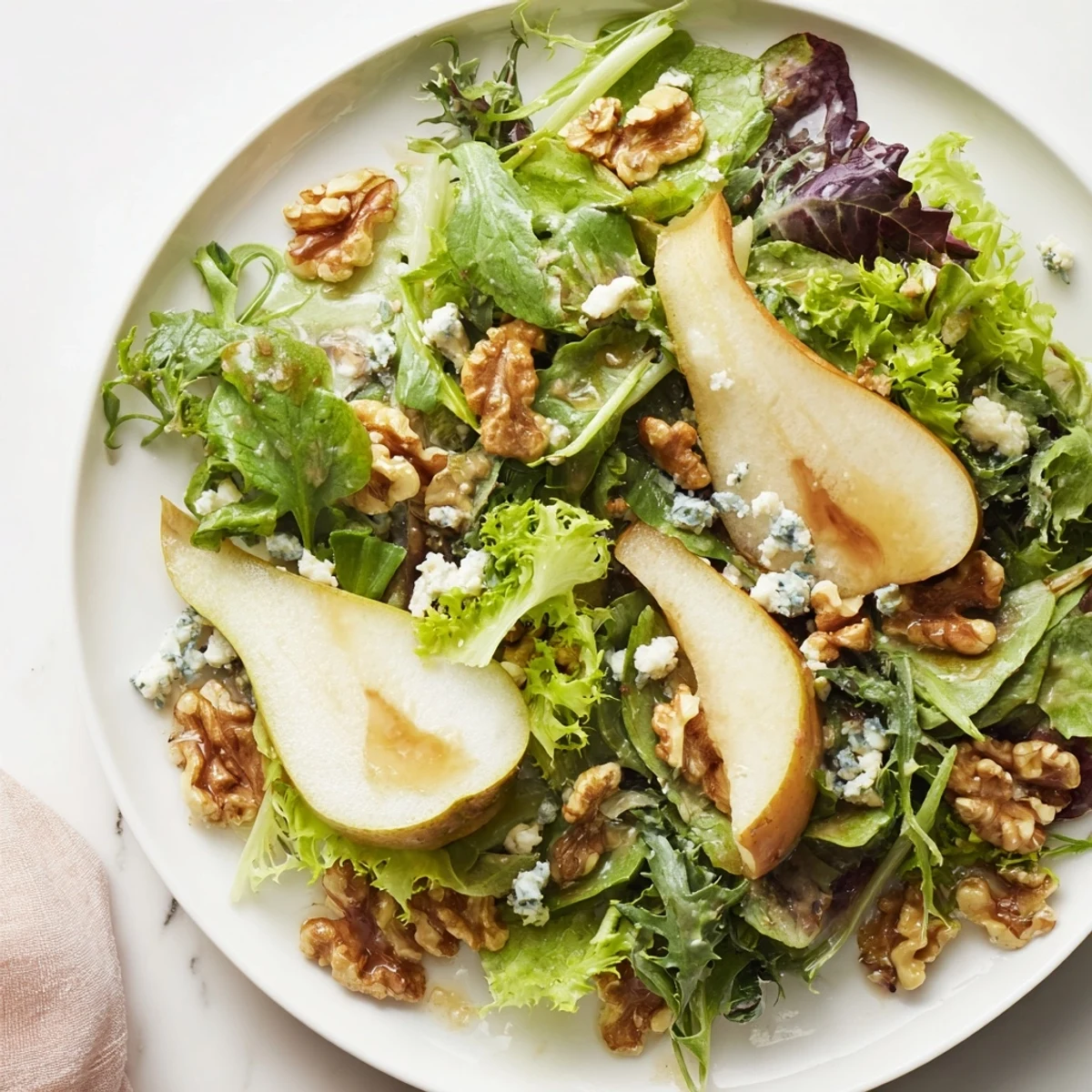 Winter Green Salad with Pear and Candied Walnuts arranged on a rustic plate with sliced pears and balsamic dressing.
