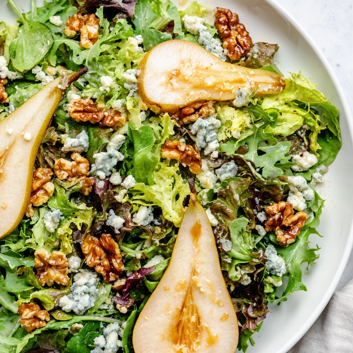 Freshly tossed Winter Green Salad with Pear and Candied Walnuts topped with creamy blue cheese, glistening in winter light.