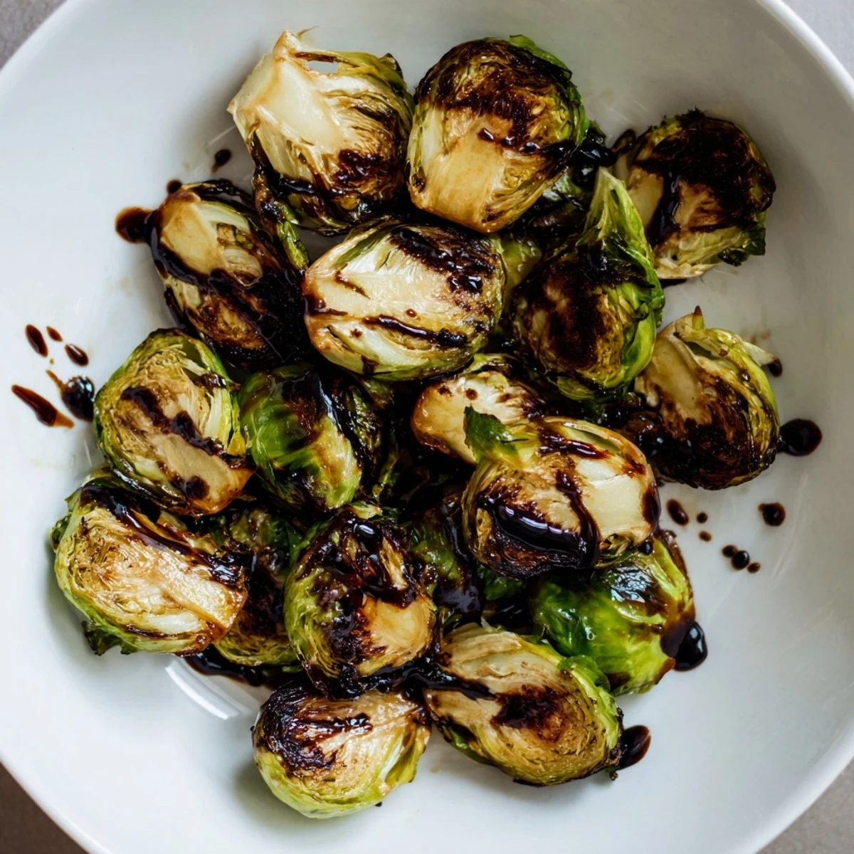 A close-up of Roasted Brussels Sprouts with Balsamic Glaze Reduction highlighting glistening glaze over tender green and brown roasted vegetables.