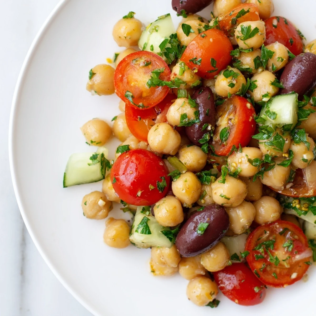 A close-up of vibrant Mediterranean Chickpea Salad with lemon vinaigrette, featuring chickpeas, tomatoes, cucumbers, and crumbled feta on a white plate.