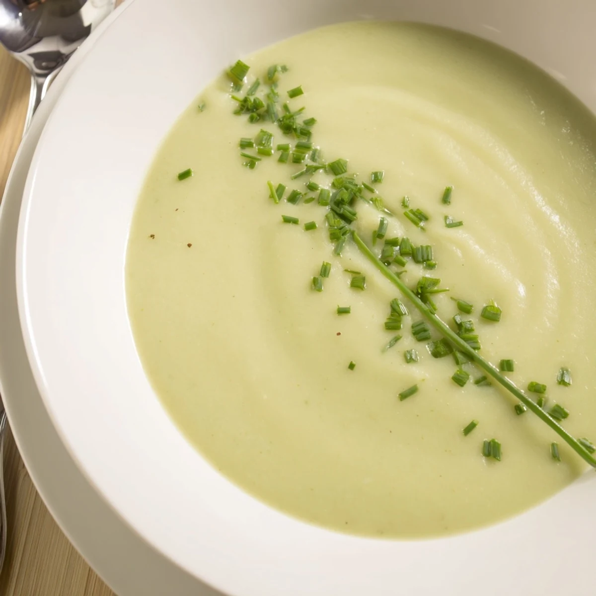 Golden Creamy Leek Soup with Potatoes, steaming in a rustic bowl, garnished with fresh chives and cracked pepper.