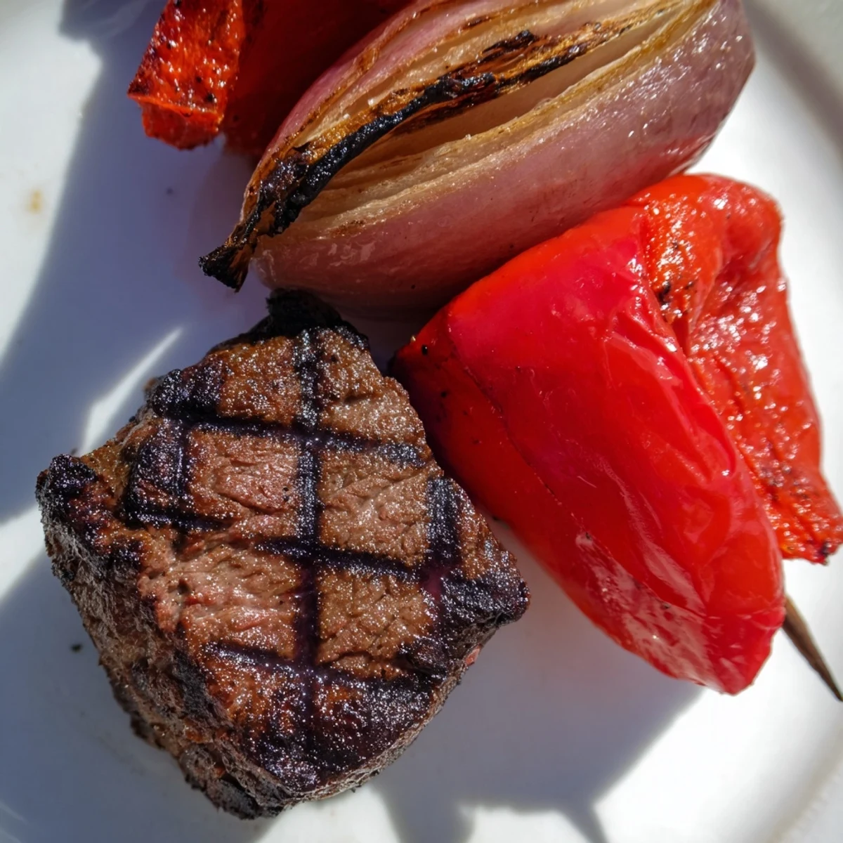 A close-up view of Beef Kebabs with Peppers and Onions, highlighting the caramelized edges of the meat and vegetables, glistening with marinade and a hint of olive oil on a dark slate background.