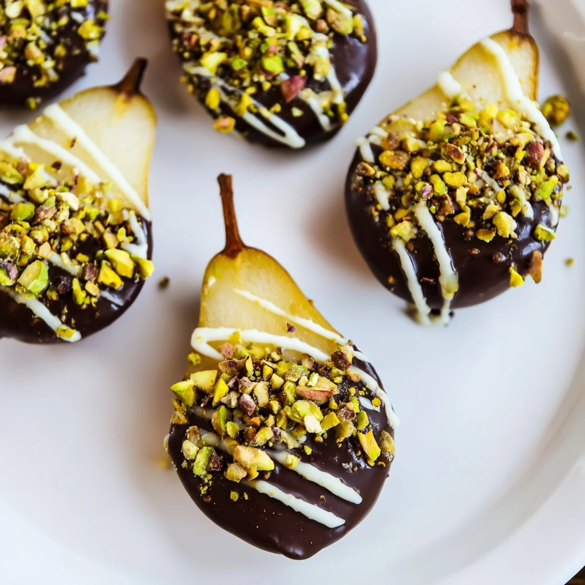 Elegant Romantic Chocolate Covered Pears glisten with rich dark chocolate, sprinkled with pistachios and sea salt on a dessert platter.