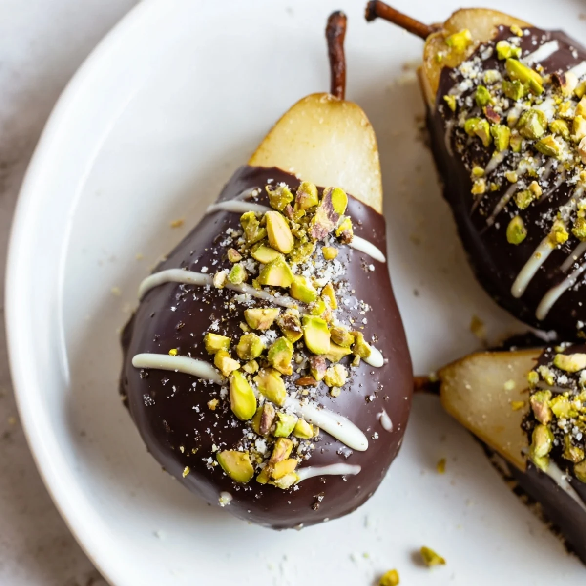 Luscious Romantic Chocolate Covered Pears topped with pistachios and salt sit on a parchment-lined tray for a decadent sweet treat.