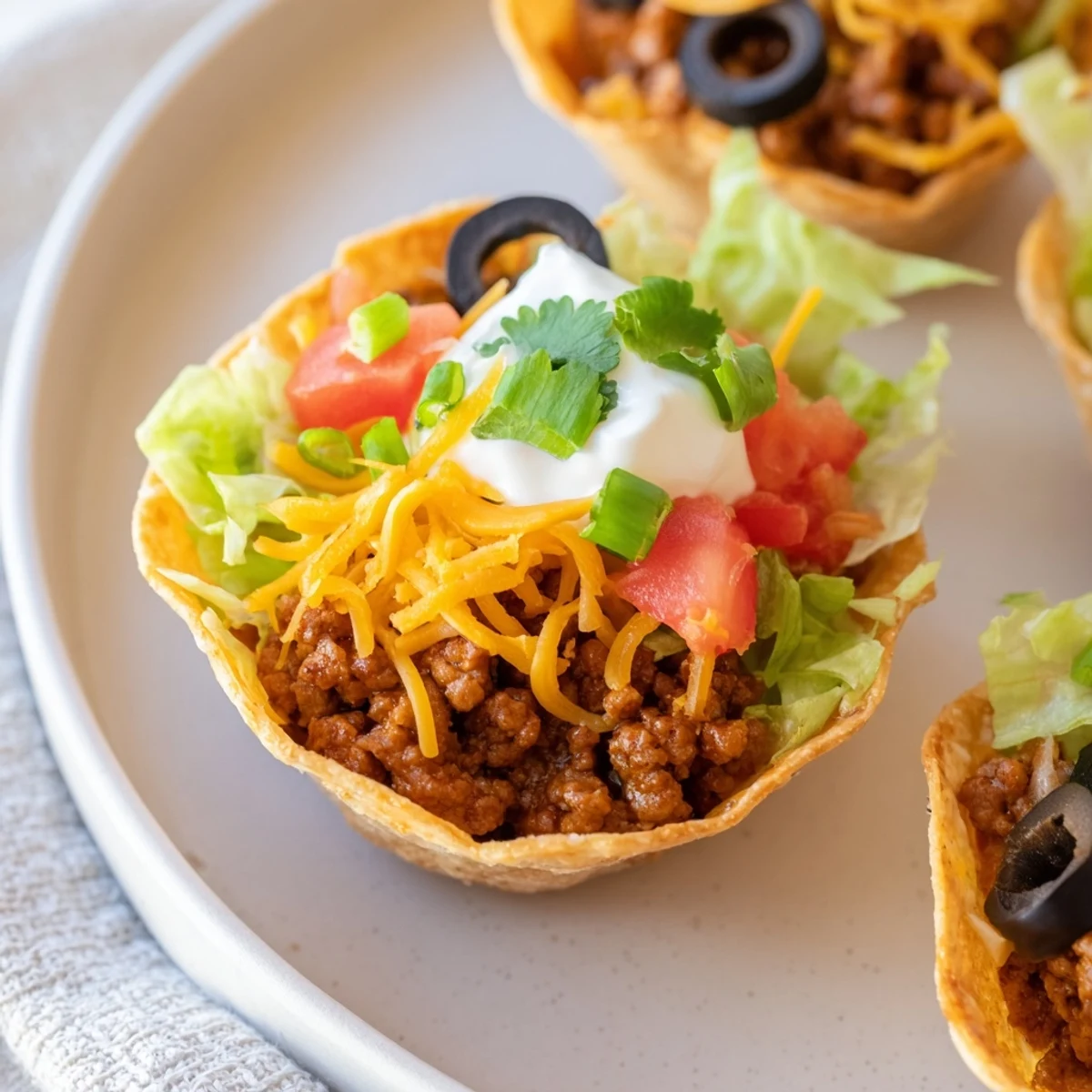 Freshly baked Touchdown Taco Cups are arranged on a platter, garnished with chopped cilantro, tomatoes, and green onions for a colorful presentation.