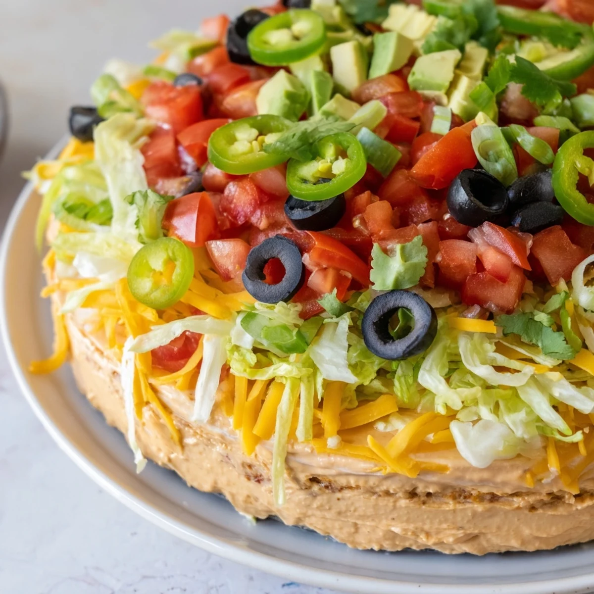 Creamy Ultimate Layered Taco Dip with tortilla chips is garnished with fresh cilantro and diced tomatoes for a cool, zesty appetizer.