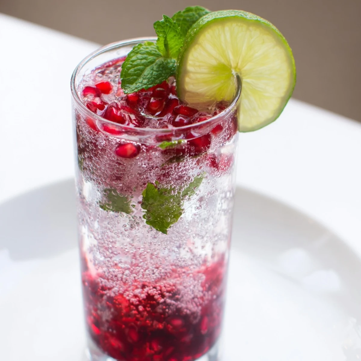 Pomegranate Fizz Mocktail with Lime, a non-alcoholic drink with sweet-tart juice, fizz, and colorful garnishes on a marble counter.