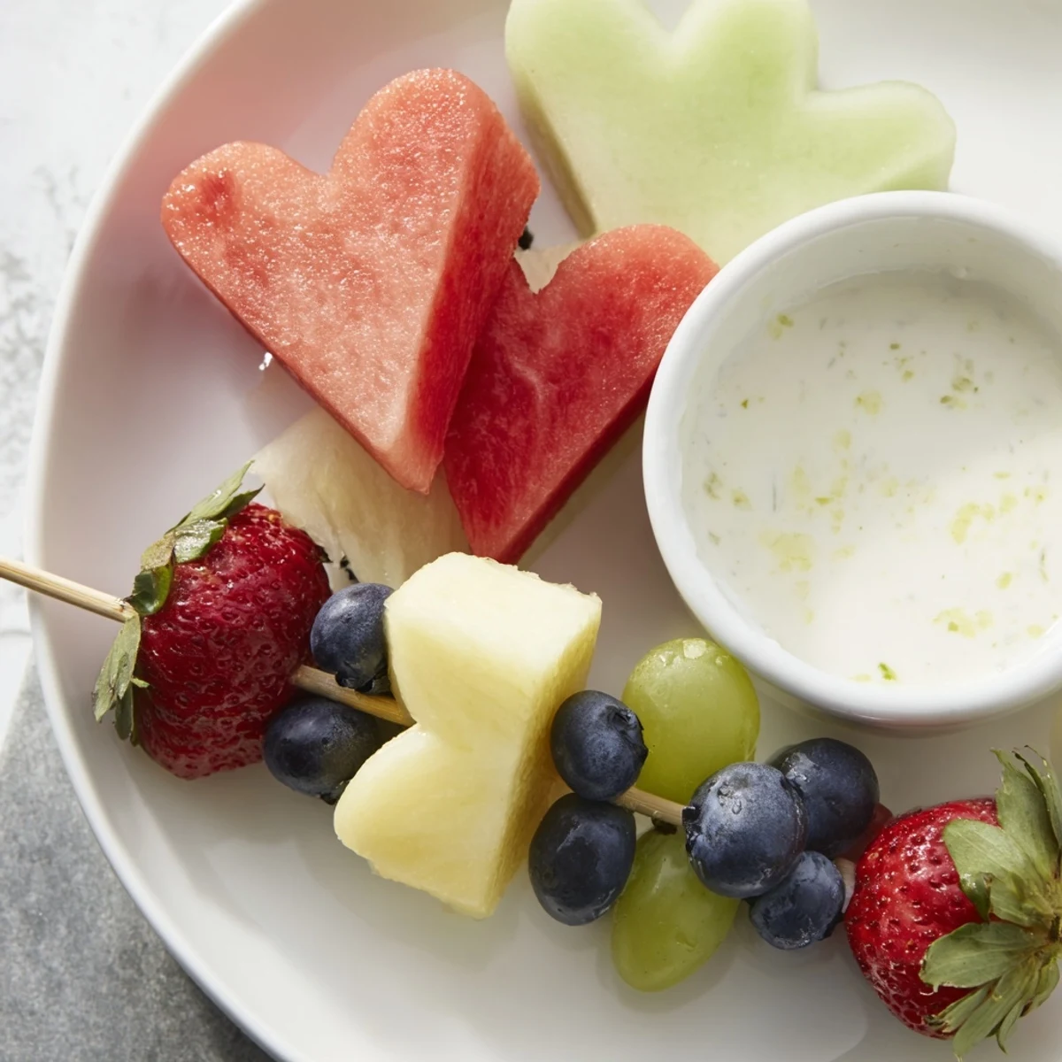 Colorful Sweetheart Fruit Skewers with Yogurt Dip arranged on a platter, topped with fresh strawberries and blueberries for a vibrant serving suggestion.