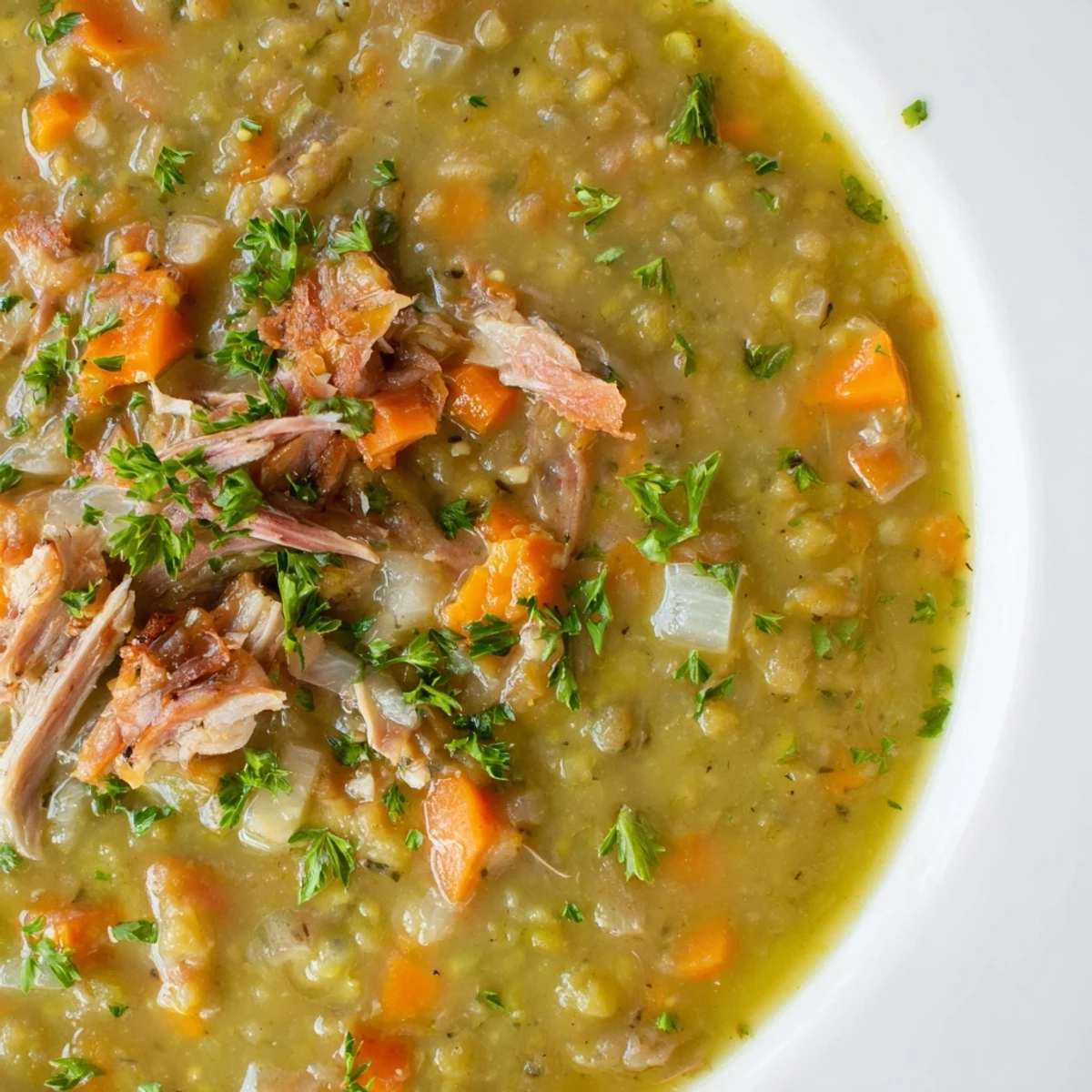 Close-up of Green Split Pea Soup with Smoked Turkey Leg, showing thick, chunky texture and a slice of crusty bread.
