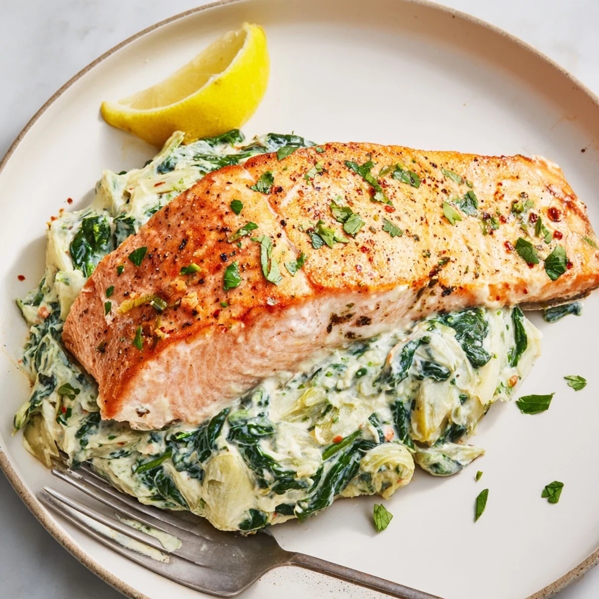 Golden-baked Creamy Spinach and Artichoke Stuffed Salmon fillets reveal a luscious green filling on a white plate with lemon wedges.