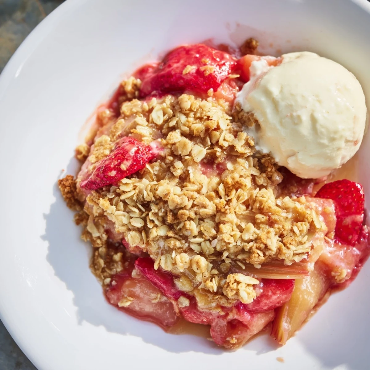 A warm slice of Strawberry Rhubarb Crisp reveals bubbling red fruit beneath a golden oat crumble topping.