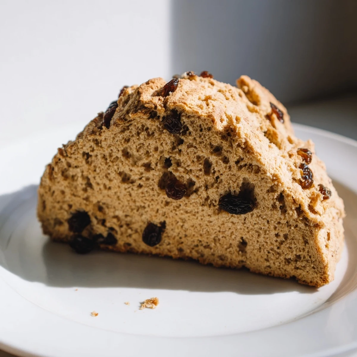 Freshly baked whole wheat Irish soda bread with currants showing a cross on top, cooling on a wire rack.