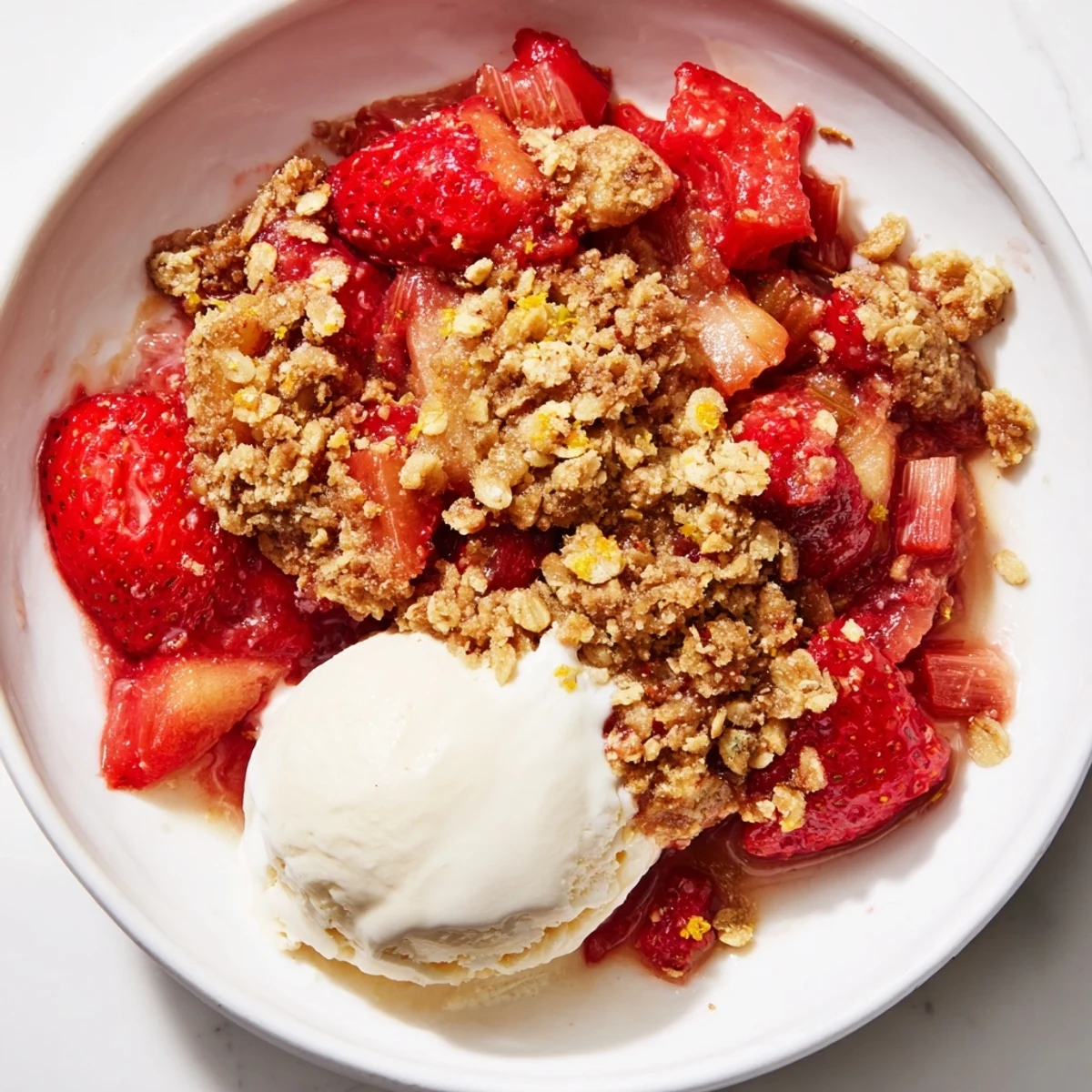 Strawberry Rhubarb Crumble baked golden, served with melty vanilla ice cream scoop.