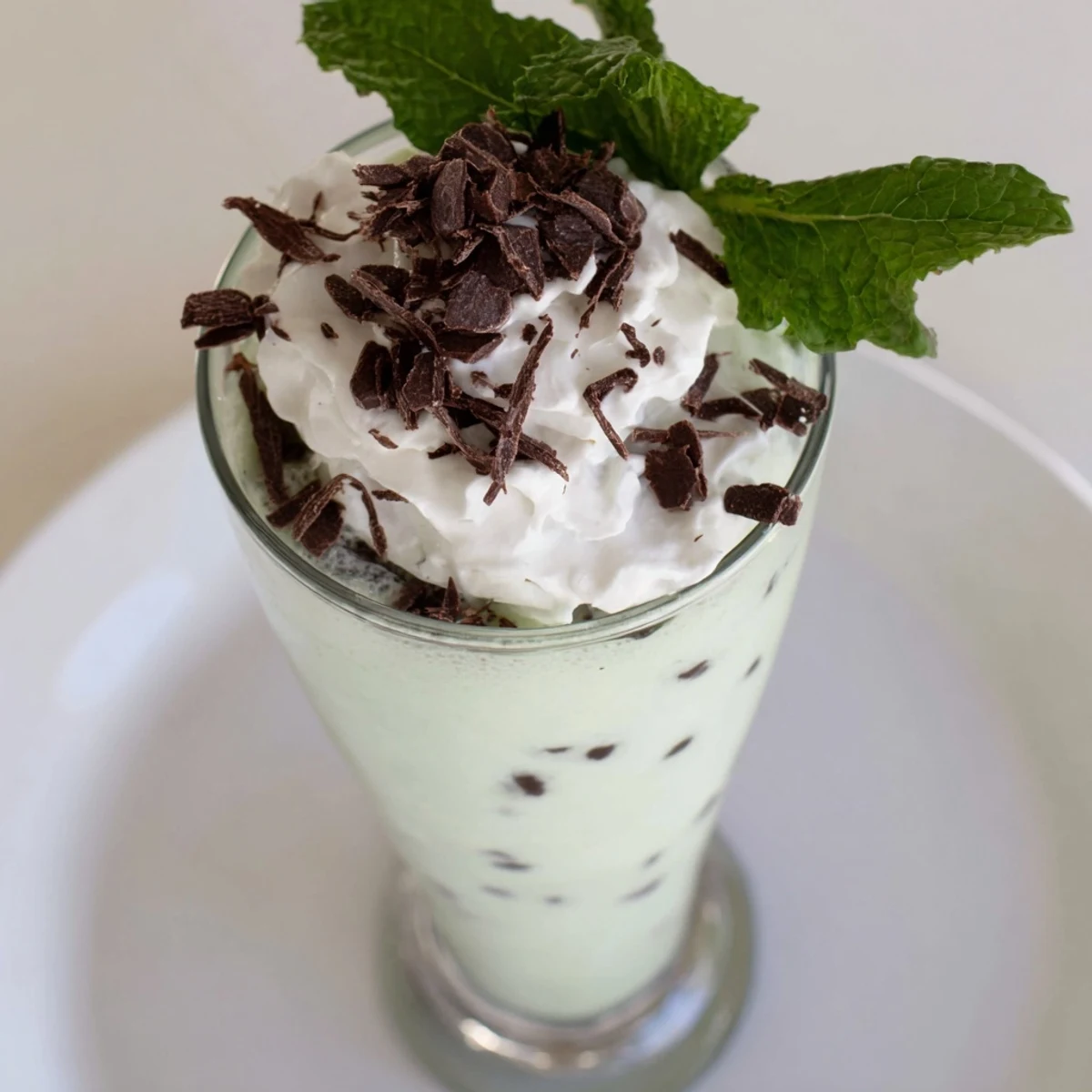 A tall glass of Mint Chocolate Chip Milkshake with whipped cream and chocolate shavings on top.