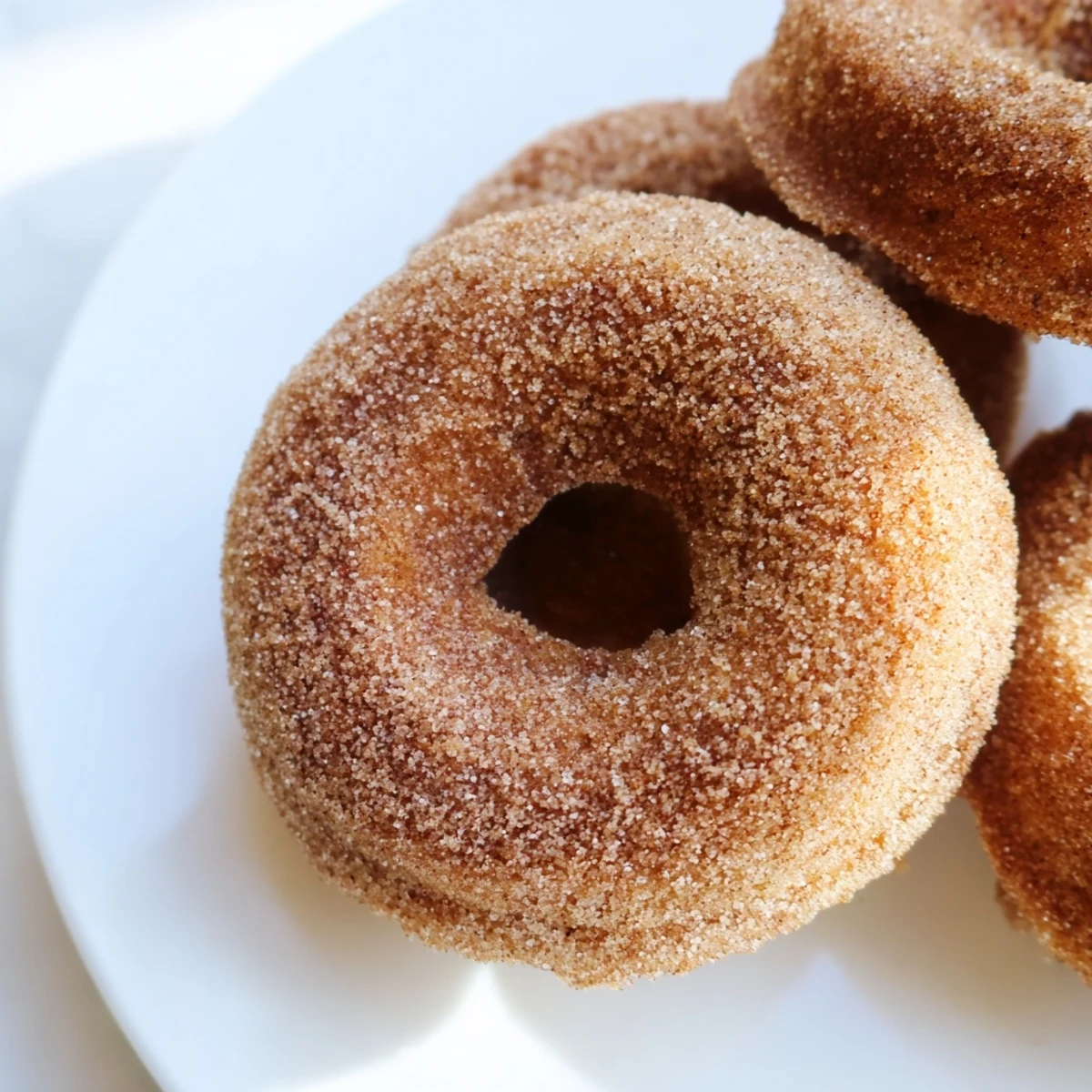 A close-up of soft, fluffy Delightful Cinnamon Sugar Donuts shows a tender crumb and rich glaze, ready to be enjoyed with a hot cup of coffee.