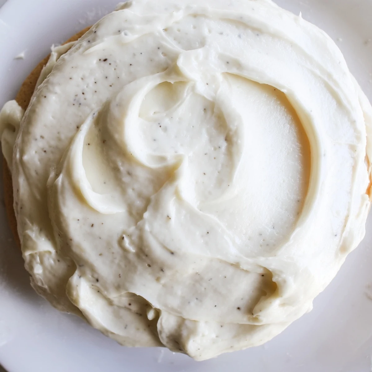 A close-up of Easy Sugar Cookie Frosting being spread on a cooled sugar cookie, showing its smooth, creamy vanilla texture.
