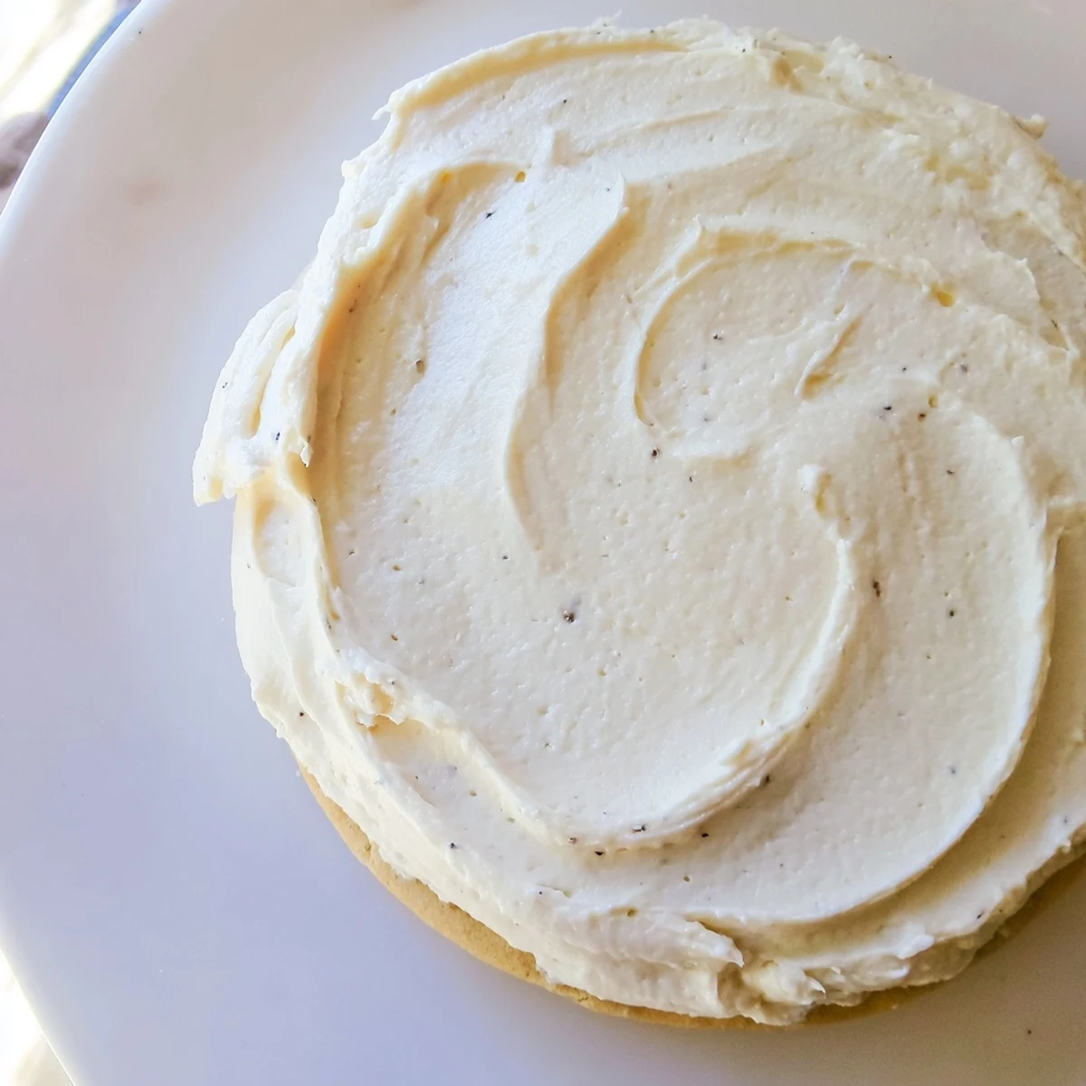 In a kitchen setting, a bowl of Easy Sugar Cookie Frosting is piped onto bright sugar cookies for colorful decoration.