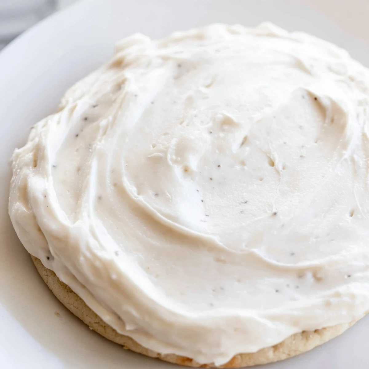 Easy Sugar Cookie Frosting in a bowl, fluffy and ready to use, with a soft crust forming on decorated cookies.