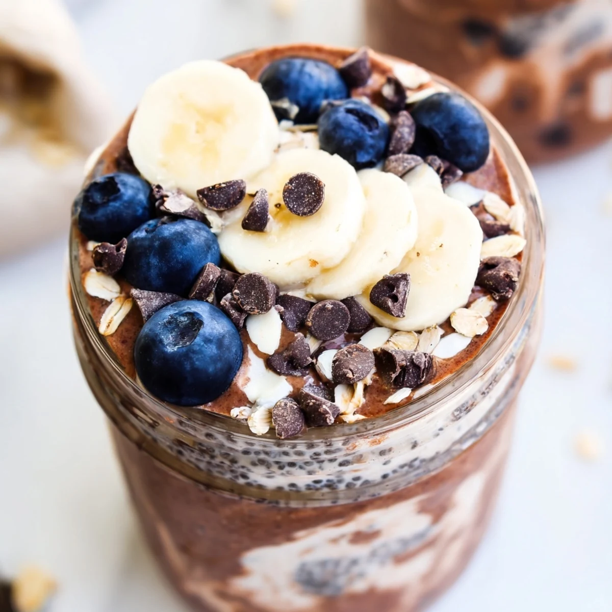 Top-down view of Ultimate Healthy Chocolate Overnight Oats in mason jars, garnished with dark chocolate chips and walnuts.