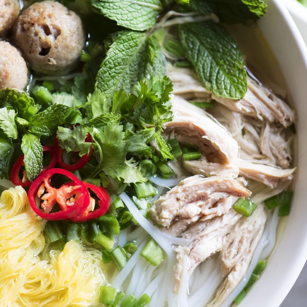 A close-up of Bun Thang featuring rice vermicelli, pork sausage slices, and a lime wedge for garnish.