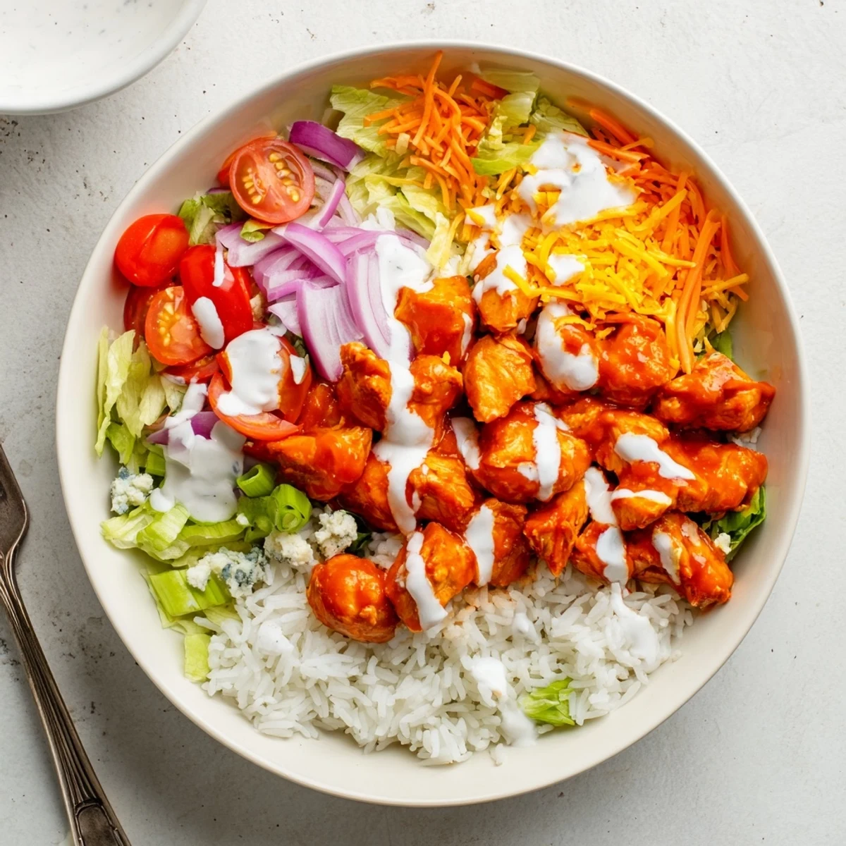 Creamy ranch drizzled over spicy buffalo chicken bowls with fluffy rice, crisp lettuce, tomatoes, and shredded carrots.