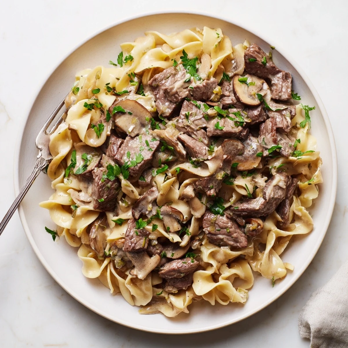 Homemade beef and mushroom stroganoff plated over egg noodles with chopped parsley topping