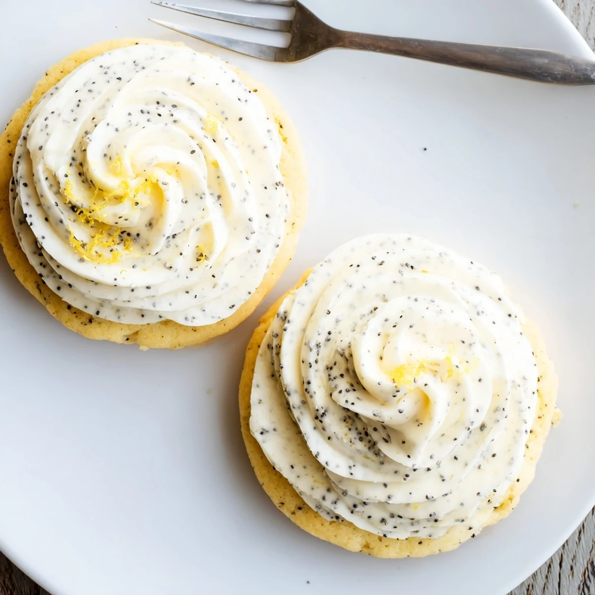 Buttery lemon poppy seed cookies topped with tangy cream cheese frosting on a white plate