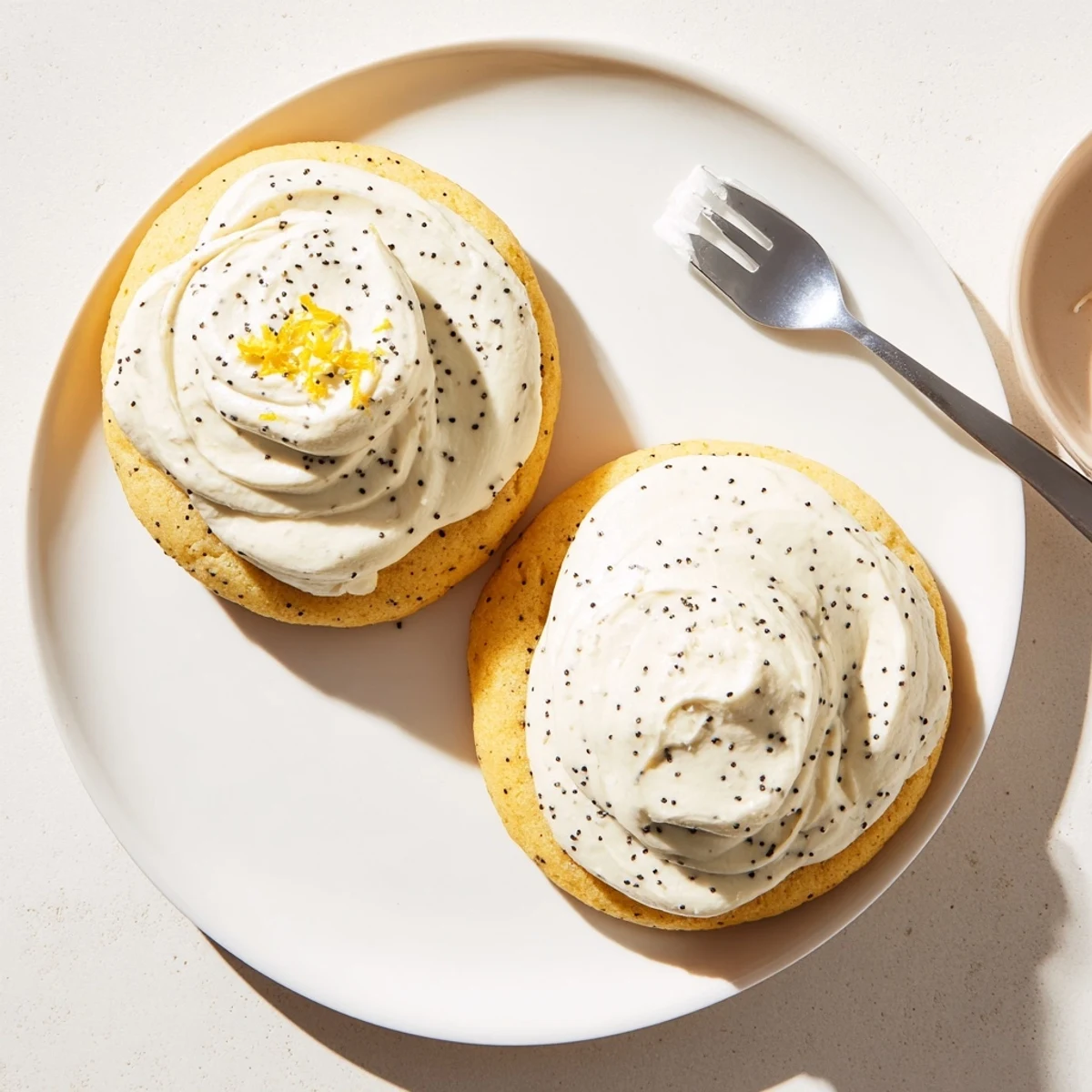 Freshly baked lemon poppy seed cookies with creamy cheesecake frosting and poppy seed garnish