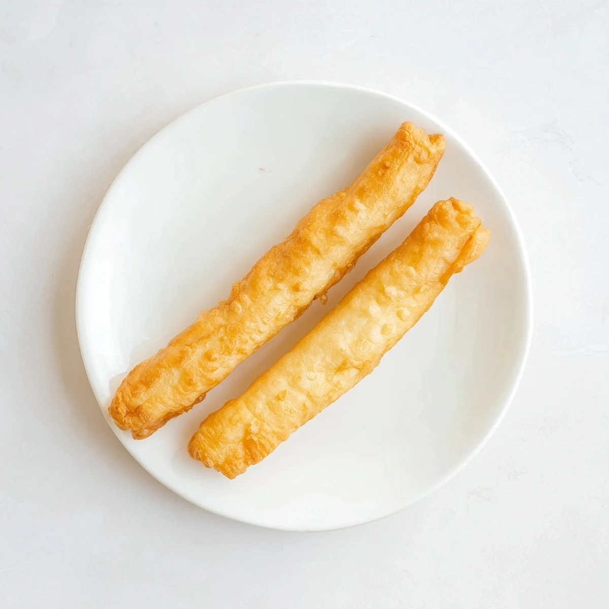 Pair of crispy Youtiao breakfast doughnuts being stretched before frying in hot oil