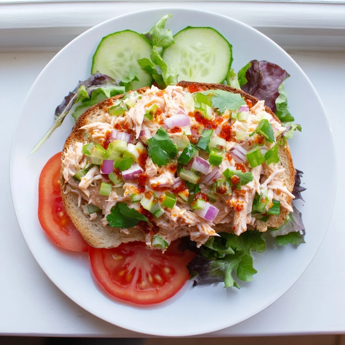 Golden chicken salad sandwich topped with fresh vegetables and spicy chili crisp drizzle