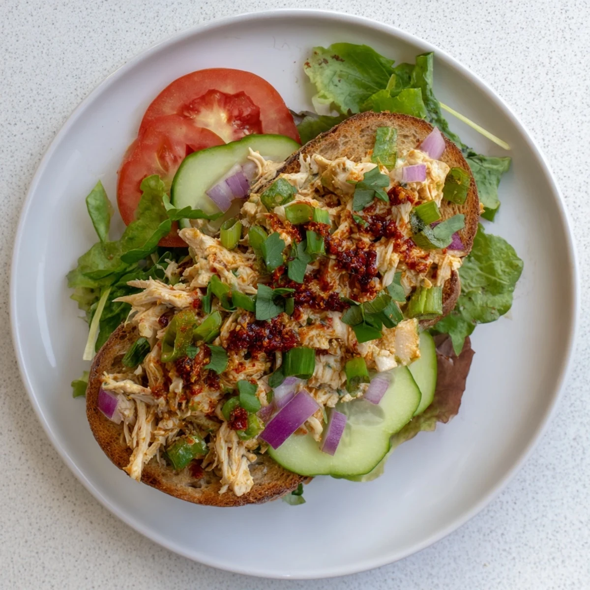 Toasted bread overflowing with creamy chicken salad mixed with crunchy vegetables and chili crisp