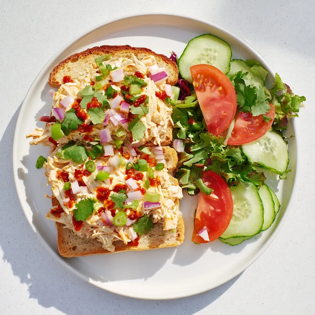 Open-faced chicken salad sandwich featuring crisp cucumber slices and aromatic spicy chili crisp topping