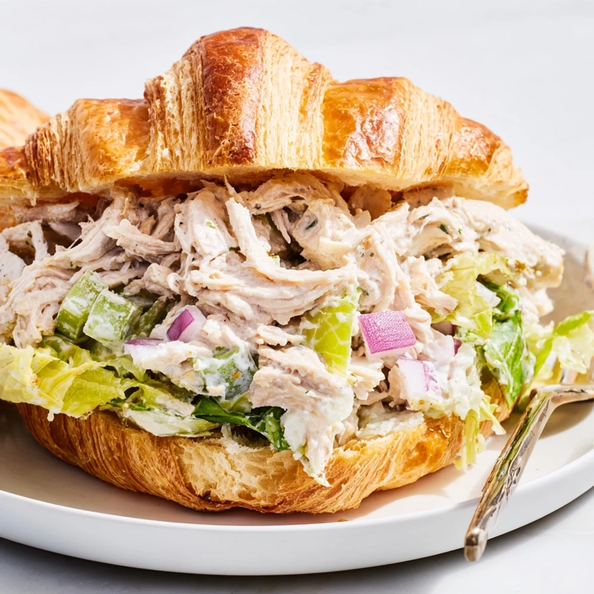 Golden croissant brimming with creamy chicken Caesar salad, crisp romaine lettuce, and Parmesan shavings