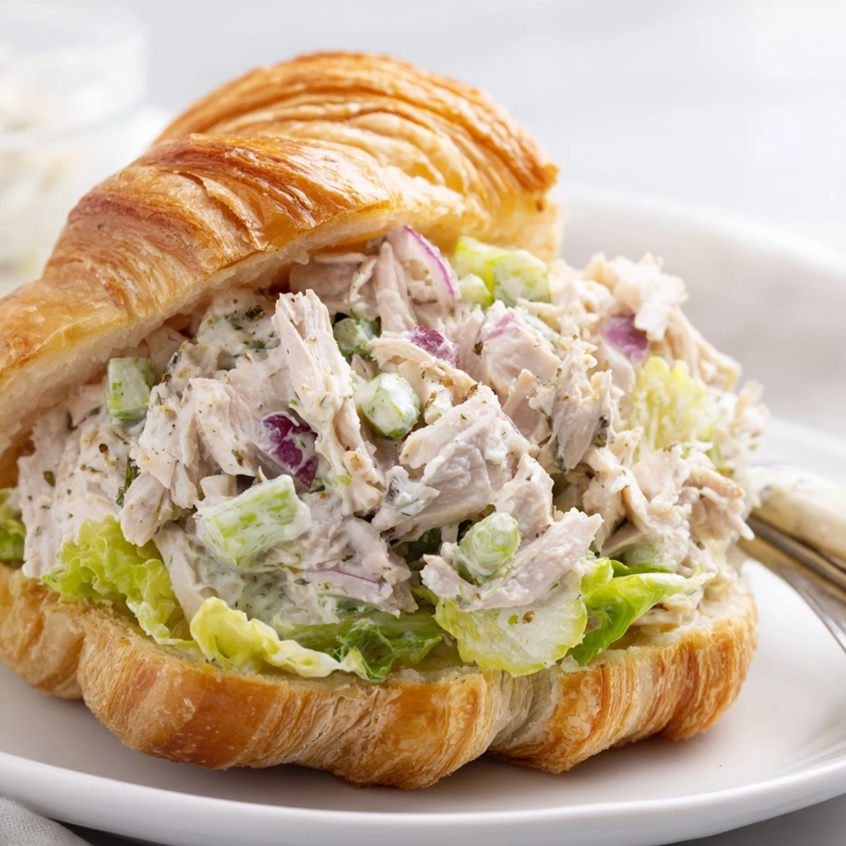 Halved buttery croissant overflowing with Caesar seasoned chicken salad, crunchy celery, and fresh lettuce
