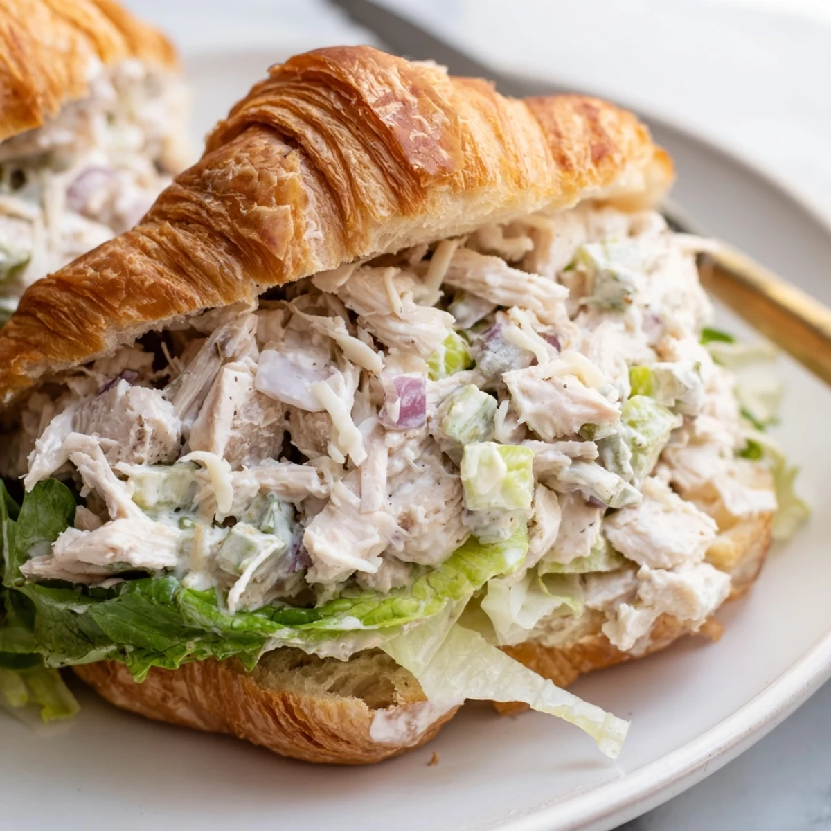 Sliced croissant sandwich stuffed with savory chicken Caesar filling, diced red onion, and romaine