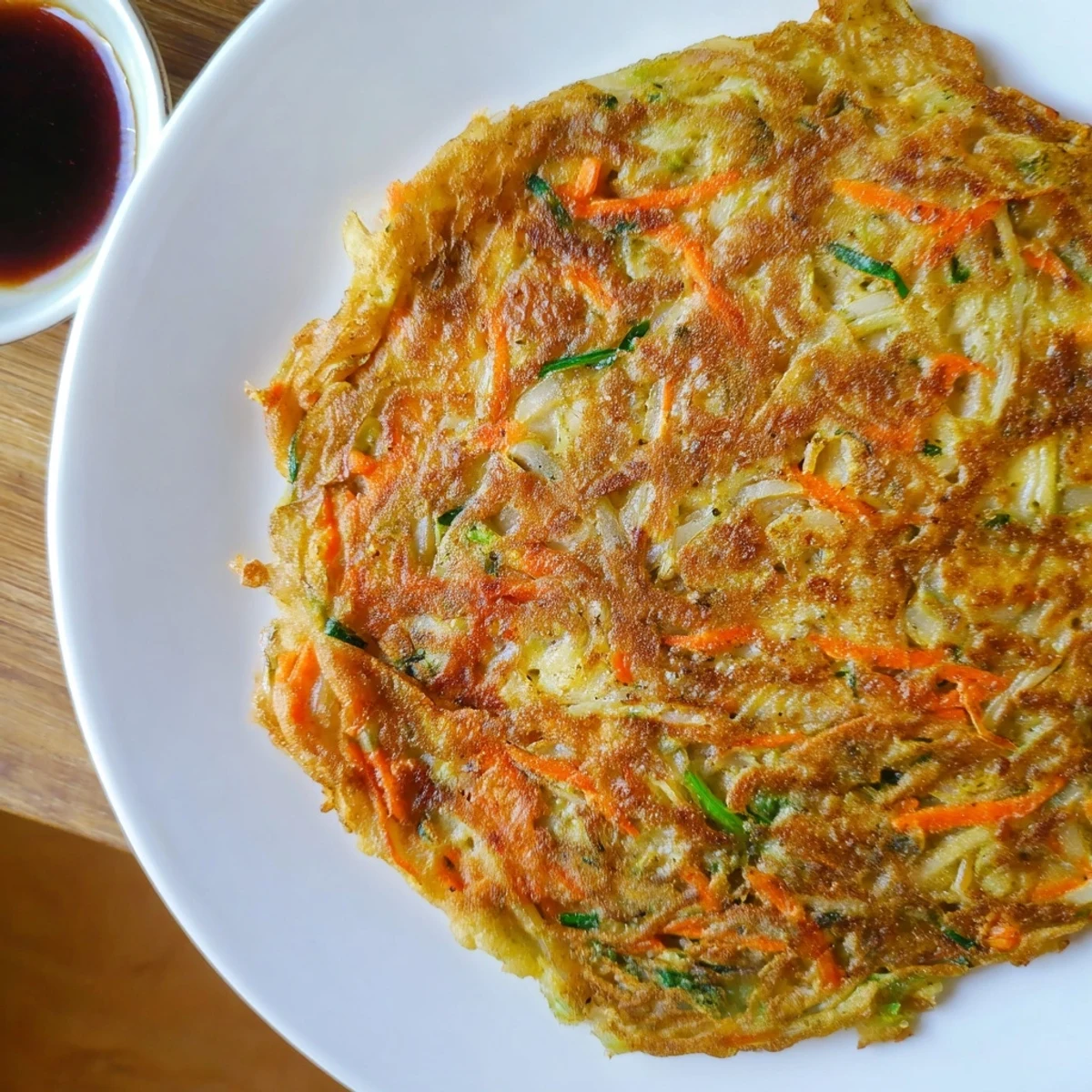 Hot Korean pancakes frying in a skillet with visible scallion pieces and carrots throughout