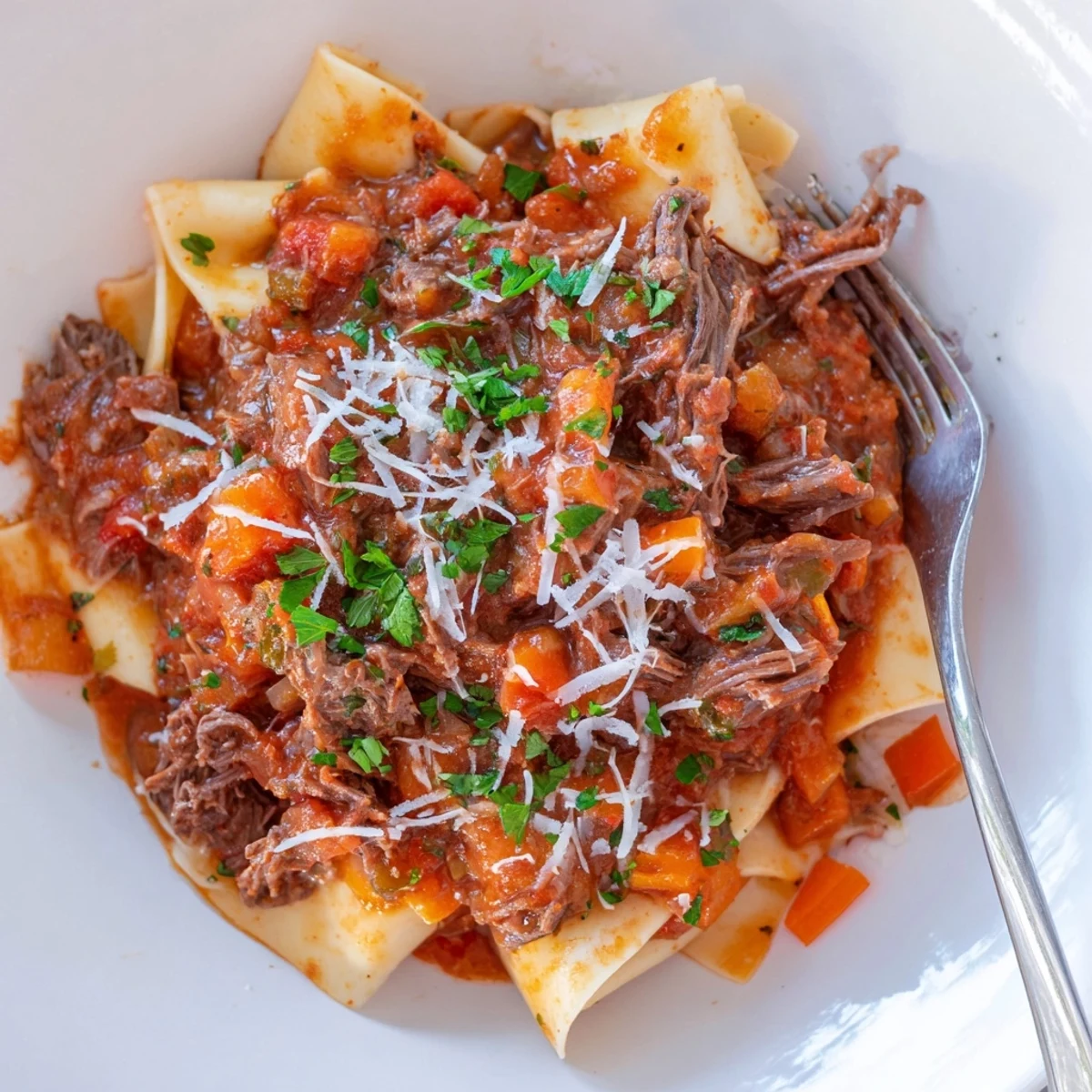 Genuine slow cooker beef ragu draped over wide noodles with fresh parsley and Parmesan garnish
