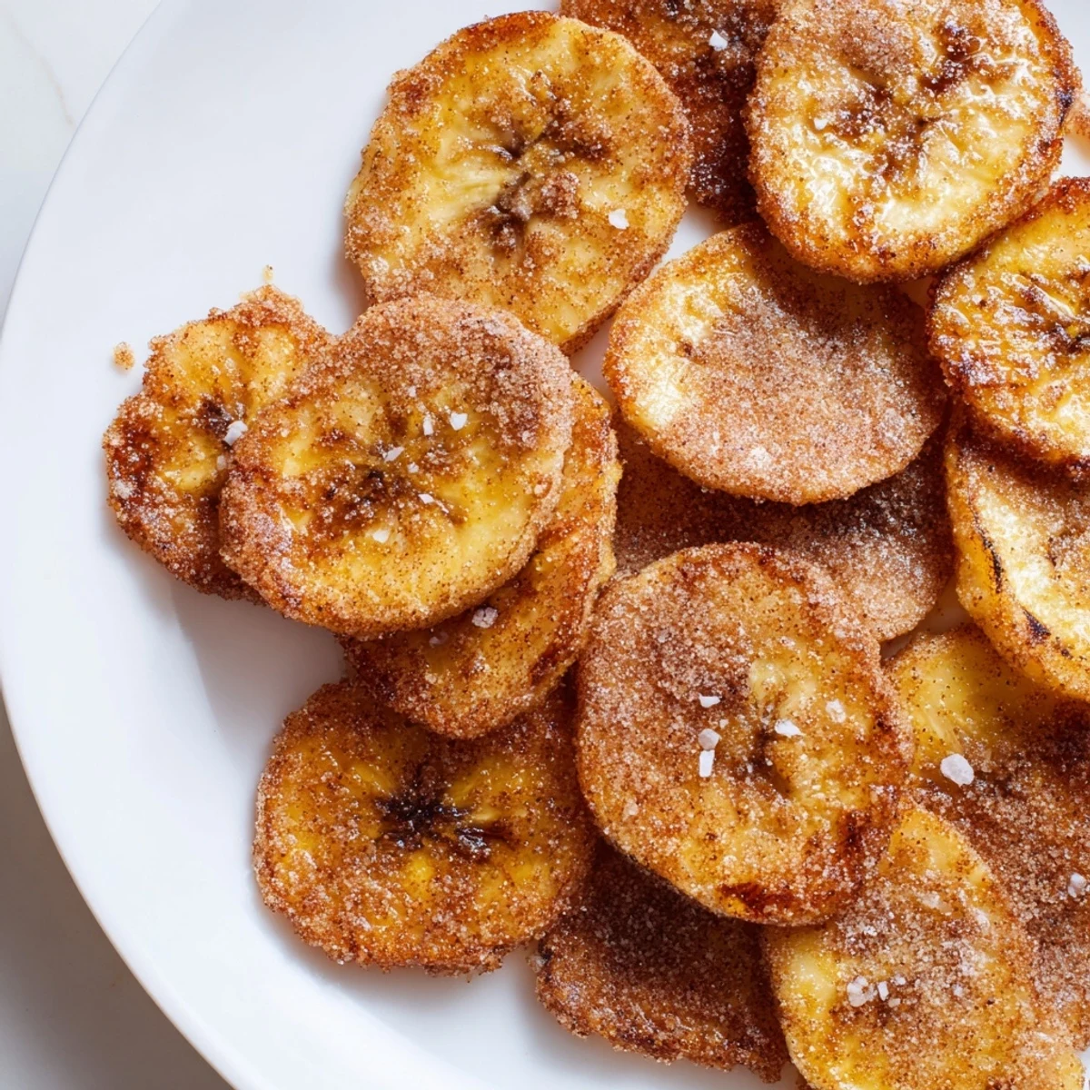 Golden cinnamon sugar air fryer banana chips arranged on a white plate