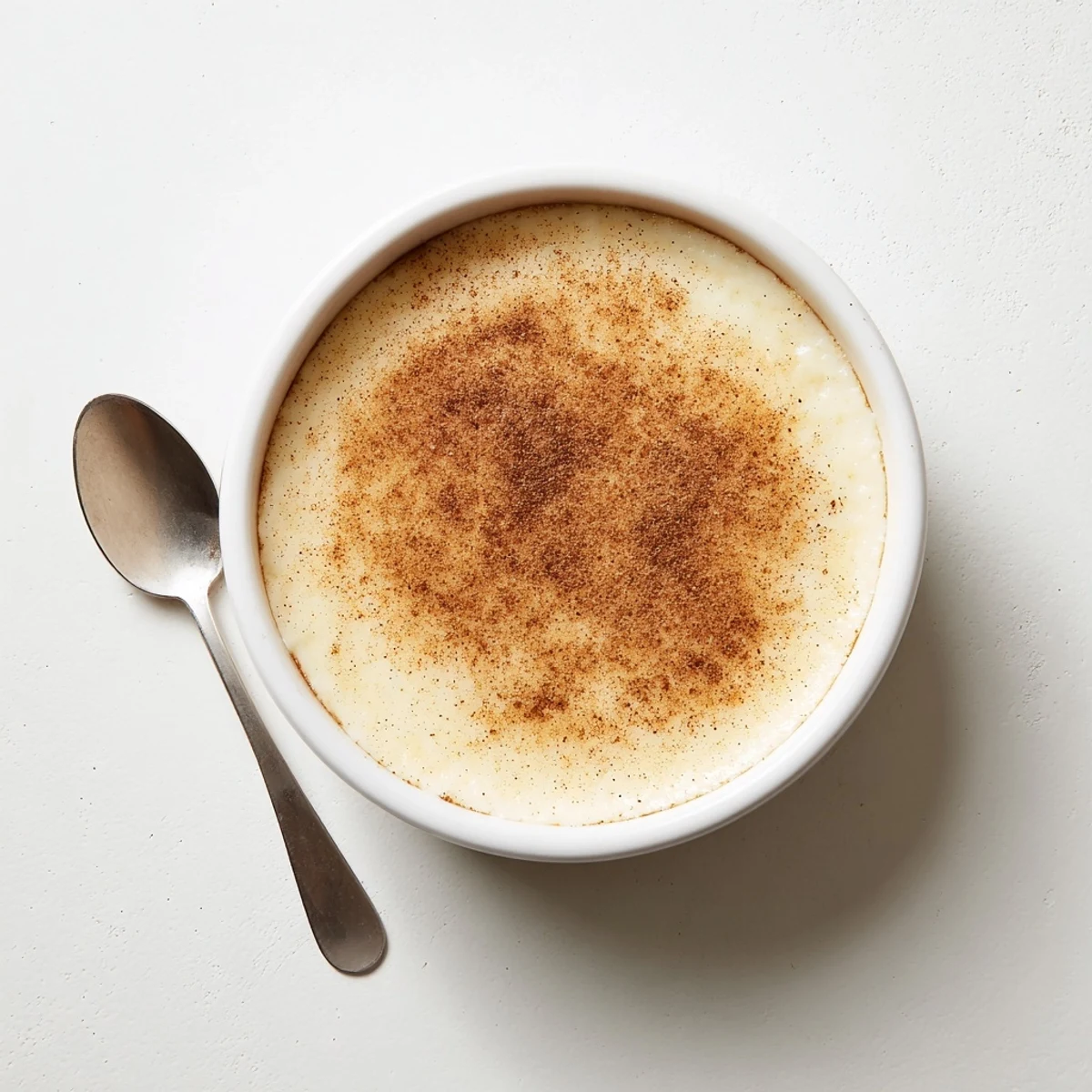 Creamy Portuguese rice custard in white ramekins topped with golden cinnamon-sugar sprinkles