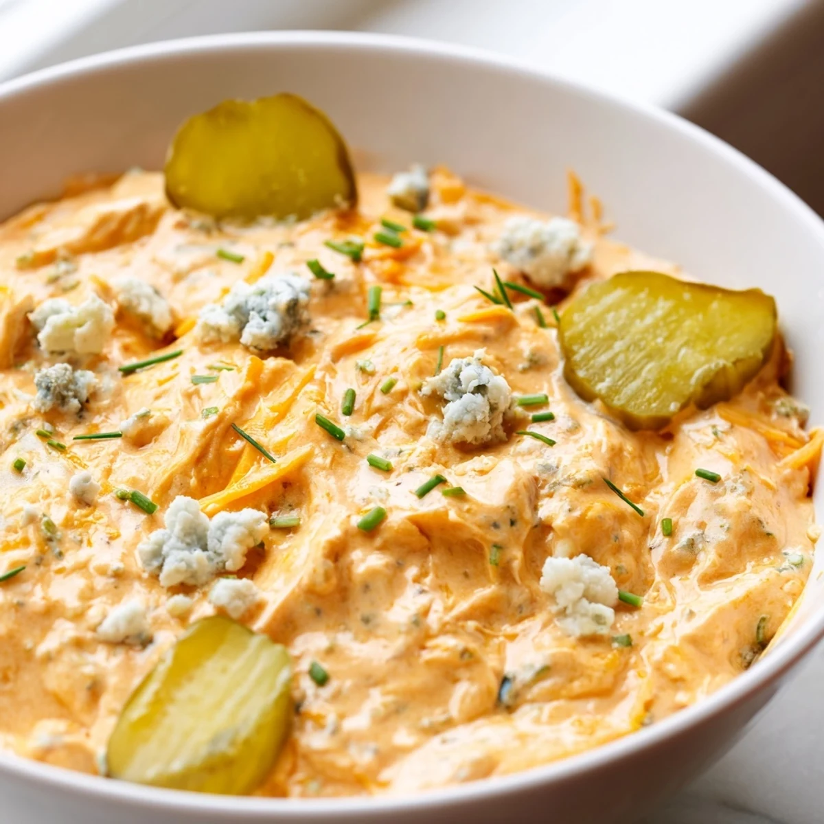 Creamy buffalo pickle dip in a serving bowl surrounded by crunchy chips and fresh veggie sticks