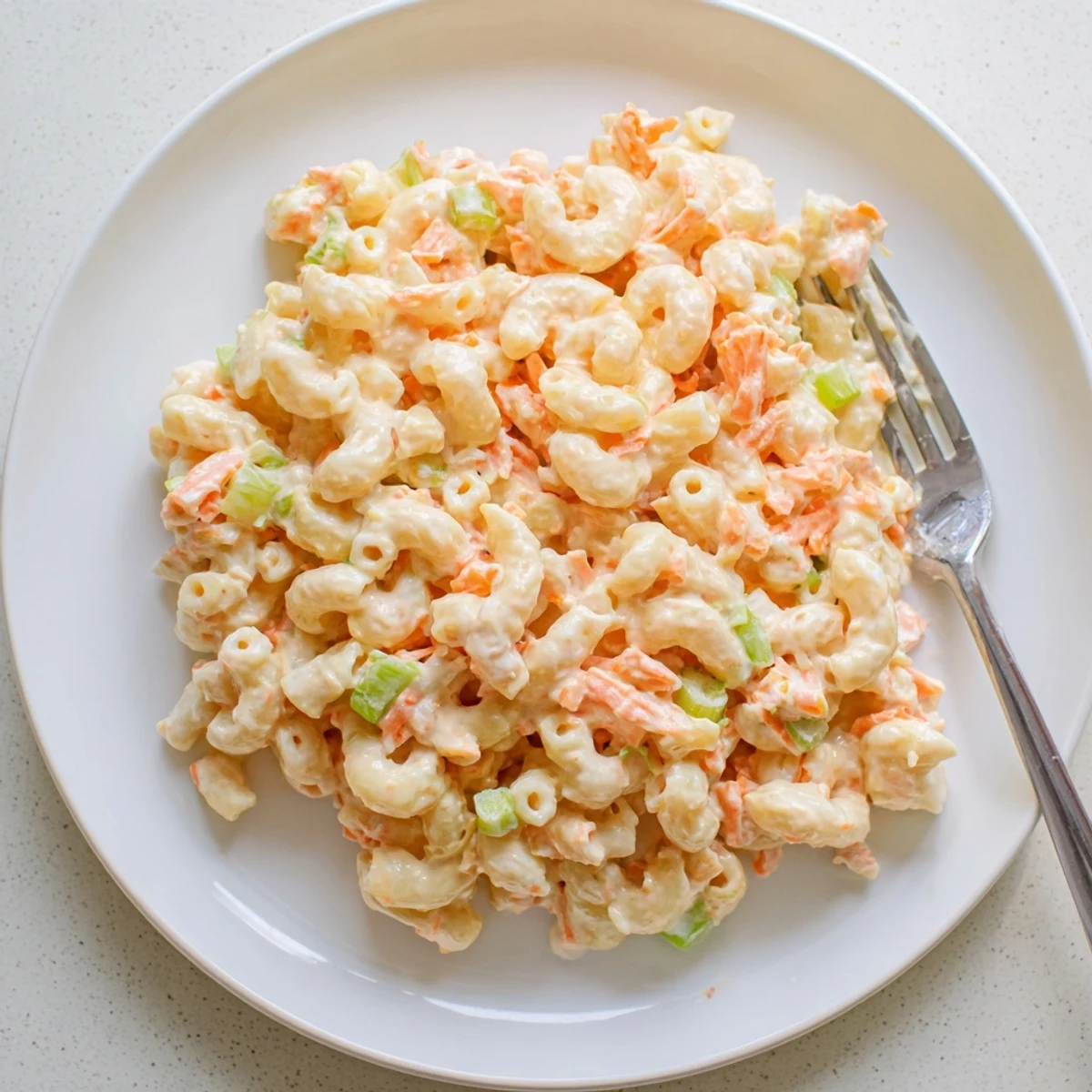 Creamy Hawaiian style mac salad piled in a bowl with colorful grated carrot and celery bits