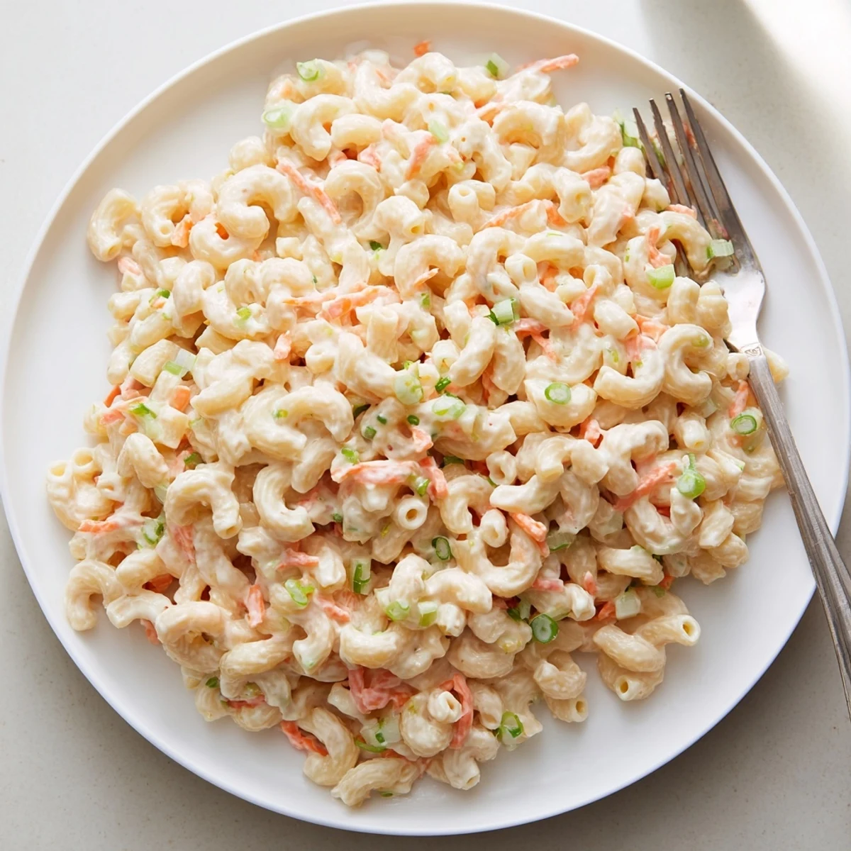 Scoop of Hawaiian style mac salad on a white plate showing its smooth velvety texture and vegetable pieces