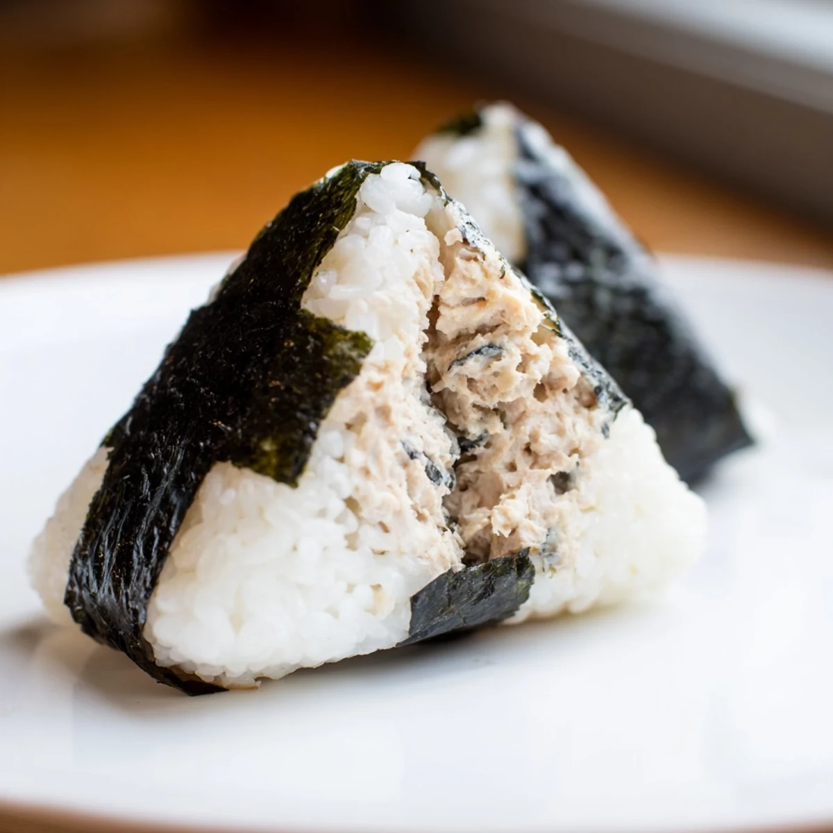 Golden triangular tuna mayo onigiri wrapped with crispy nori strips on a white plate