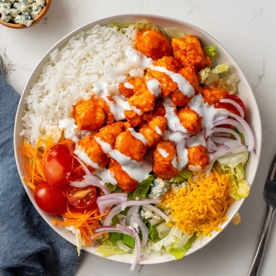 Flavor-packed buffalo chicken bowls feature cool ranch, crunchy vegetables, melted cheddar, and green onions for a hearty meal.